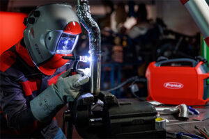 Practical example of the Fronius Artis: Portable Lightweight TIG Welder being used to weld parts whilst wearing a grey with red stripe welding helment and equipment from Fronius