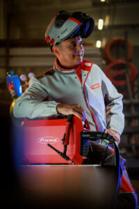 Welder Wearing Fronius Welding Protection Gear Leaning On Fronius Artis TIG Welder